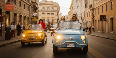 Turisti a bordo di convertibili Fiat 500 vintage che percorrono una strada nel centro di Roma