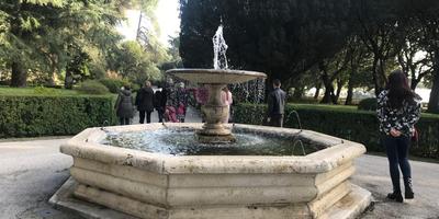 Fonte octogonal de pedra cercada por visitantes nos jardins das Vilas Pontifícias em Castel Gandolfo